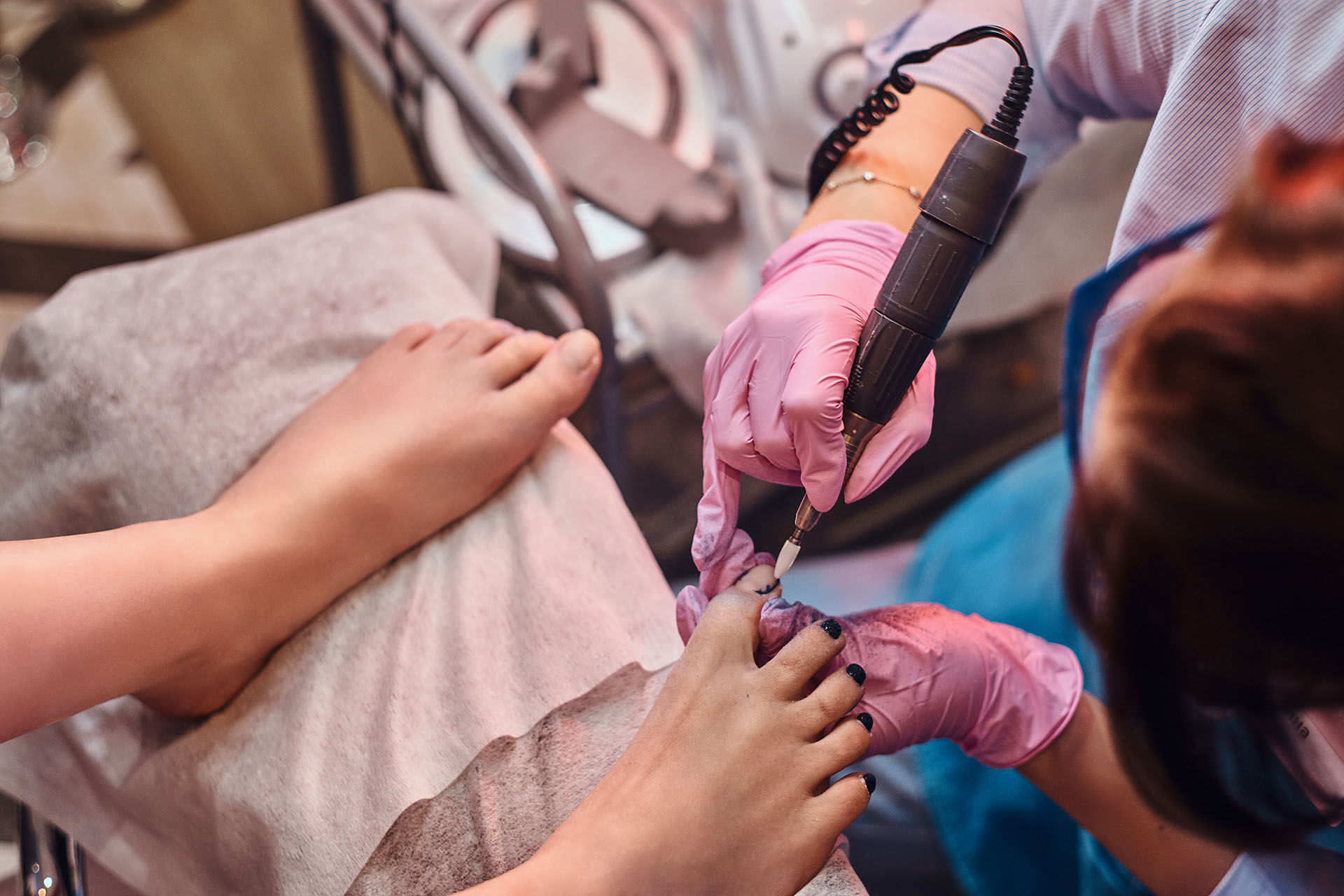 Young cheerful nail master is working on customer's toe nails at her own manicure studio.